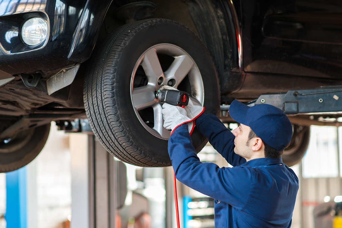 A technician looks at a raised vehicle's front tire.