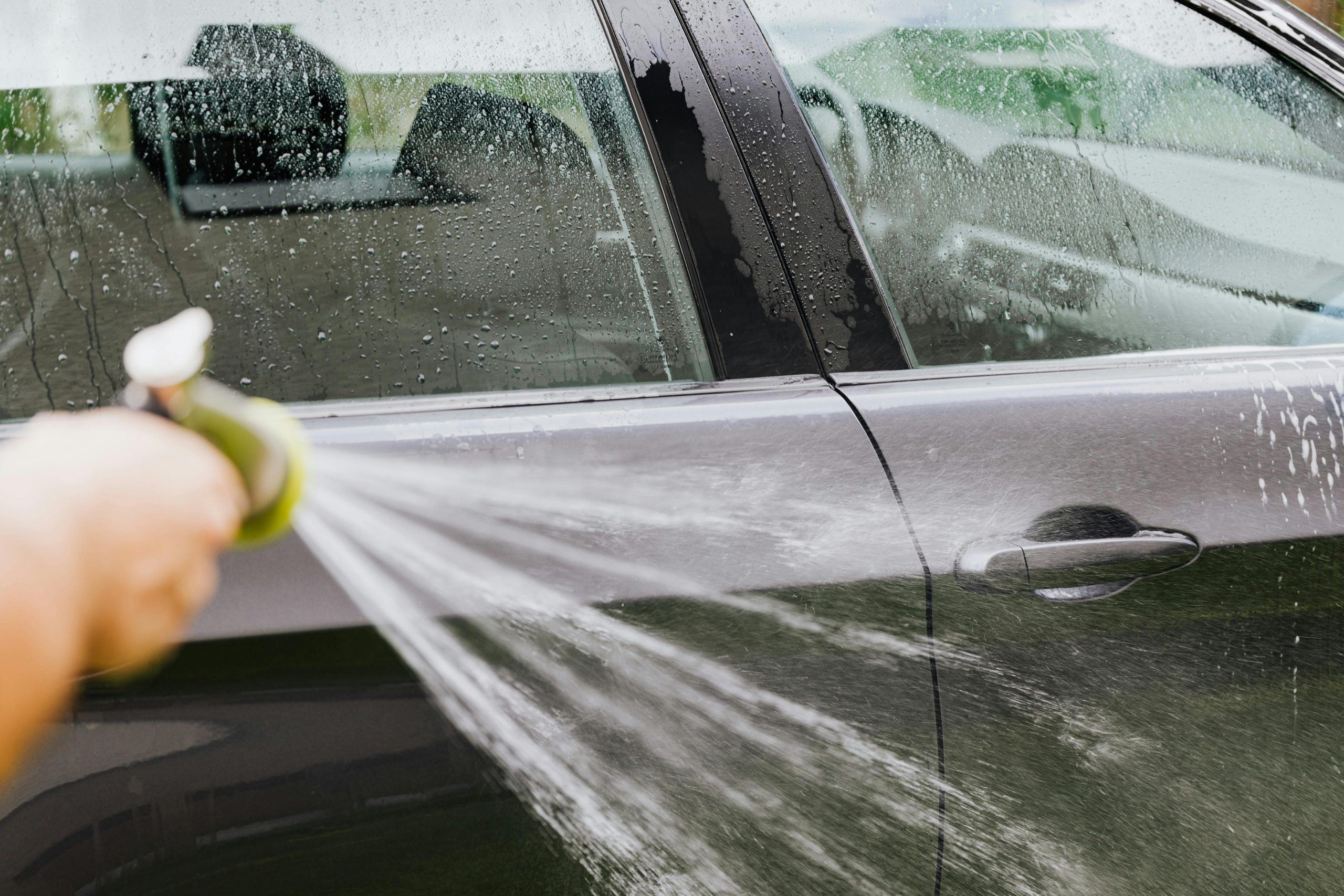 A car owner washes their car in the summer.
