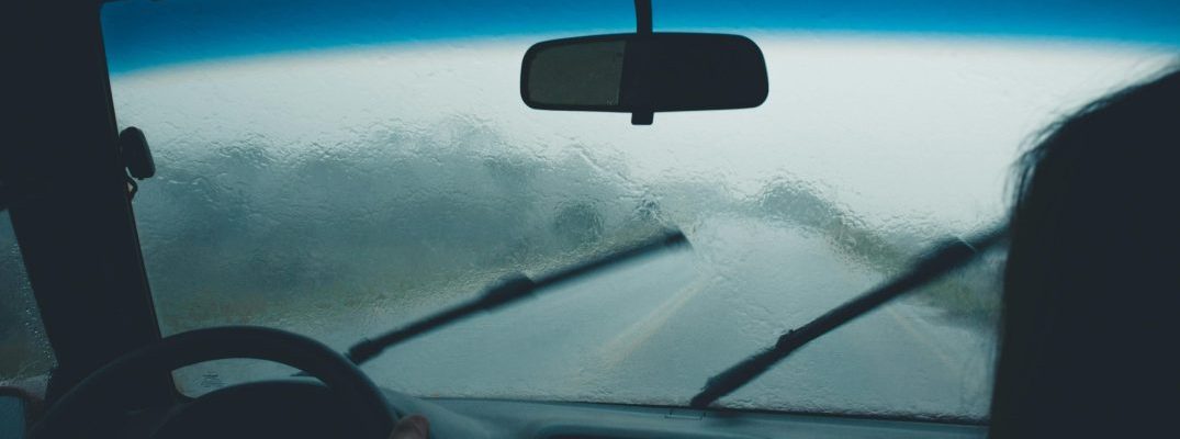 A driver uses their windshield wiper blades on a foggy windshield.